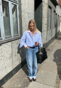 Μπλε και άσπρη ριγέ πουκάμισο με υπερμεγέθη μανίκια, ανοιχτό μπλε τζιν με διπλωμένα μπατζάκια και μαύρη τσάντα ώμου. Παπούτσια με πουά.