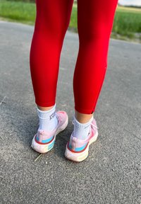 Červené sportovní legíny v kombinaci s růžovými teniskami, které mají světle modré a bílé prvky. Bílé ponožky viditelné nad teniskami.