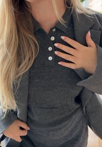 Grijze, wollen blend, button-up polo met een zachte textuur. Beschikt over drie knopen en geribbelde manchetten, gecombineerd met een grijze blazer.