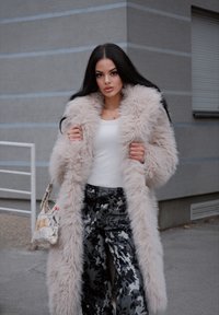 Hosszú, bolyhos bézs műszőrme kabát, fehér, testhez simuló felső és széles lábú fekete virágmintás nadrág. Kiegészítők között szerepel egy mintás kézitáska.