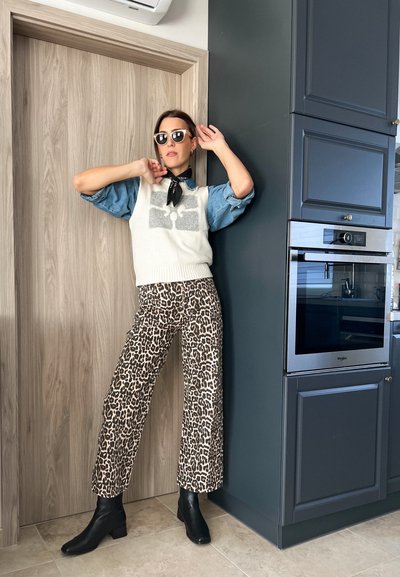 Suéter blanco de punto con diseño gráfico sobre una camisa de mezclilla, combinado con pantalones recortados de leopardo y botas negras hasta el tobillo.