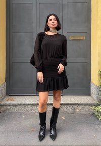 Μαύρο φόρεμα με διαφανείς μακριές μανίκες, σμιλεύτησε μέση και ριχτό στρίφωμα. Συνδυασμένο με μαύρες μπότες έως το γόνατο και μεταλλικό κολιέ.