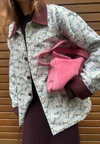 Blommig quiltad jacka med ljusblå bakgrund och mörkt vinröd krage, kombinerad med en liten rosa mockaväska.