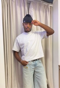 Witte cropped t-shirt, lichtblauwe wijde jeans. Geaccessoireerd met een gouden veiligheidsspeld en een parelkettinggordel. Zwarte beanie op het hoofd.