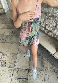 Flerfarget, ermeløs minikjole med snorfront, med blomsterprint i rosa, grønt og lilla, parret med hvite joggesko.