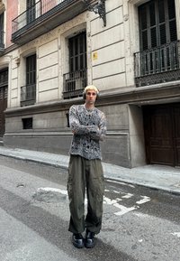 Grijze, oversized gebreide trui met een losse, versleten uitstraling; olijfgroene cargobroek; dikke zwarte platform schoenen; stedelijke straatsetting.
