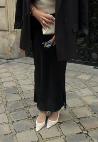 Gonna nera lunga con uno spacco laterale, abbinata a un maglione color crema e a un cappotto nero oversize. Tacchi bianchi a punta e una piccola borsa color crema.