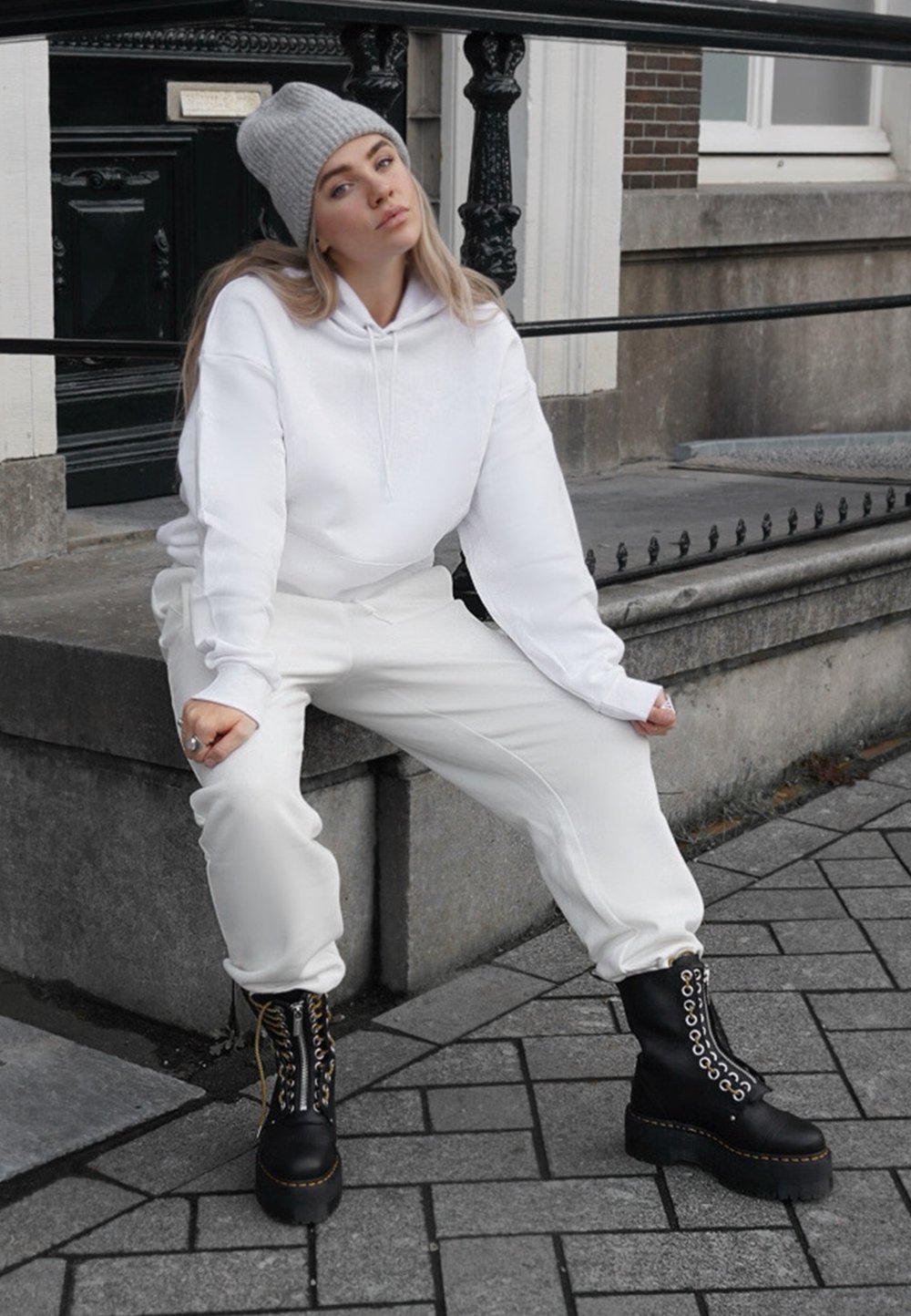 White hoodie and sweatpants, teamed with chunky black lace-up boots adorned with metallic eyelets. The model also wears a light grey beanie.