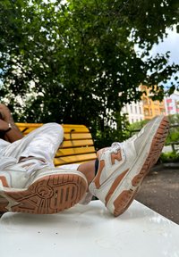Zapatillas blancas y naranjas con un diseño robusto, que presentan una suela texturizada, materiales de malla y cuero, descansando sobre un banco.