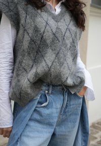 Grijze, fuzzy gebreide vest met een V-hals, voorzien van een diamanten patroon in donkerblauw, gecombineerd met lichtblauwe losse denim jeans.