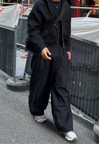Sudadera negra de gran tamaño con cremallera y pantalones anchos de rayas verticales negras, combinados con zapatillas gris claro, caminando por la calle.