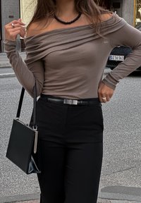 Καφέ μπλούζα ανοιχτού ώμου με μακριά μανίκια, συνδυασμένη με μαύρο παντελόνι και μαύρη τσάντα. Υφαντό ύφασμα με σχεδίαση που δημιουργεί ρίγος.
