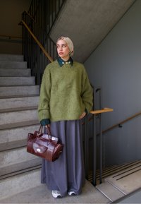 Zelený chlupatý svetr, tmavě zelená košile s límečkem, šedé široké kalhoty, hnědá kabelka a bílé tenisky. V pozadí jsou schody a zábradlí.