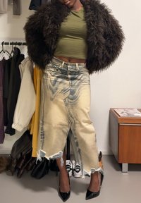 Manteau en fausse fourrure marron, crop top vert olive, jupe en denim déchiré avec ourlet effiloché, et escarpins noirs à bout pointu, avec une esthétique moderne.