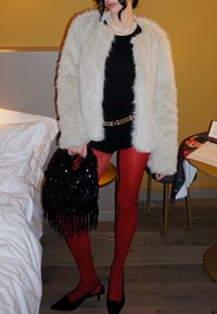 Casaco de pelúcia creme, bodysuit preto, collants vermelhos, saltos pretos, cinto embellido, mala preta com franjas, colar de pérolas em camadas.