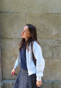 Grauer Reißverschluss-Hoodie über einem marineblauen Oberteil, kombiniert mit einem karierten Rock. Der Stoff wirkt weich; bemerkenswerte Details sind ein Reißverschluss und Taschen.