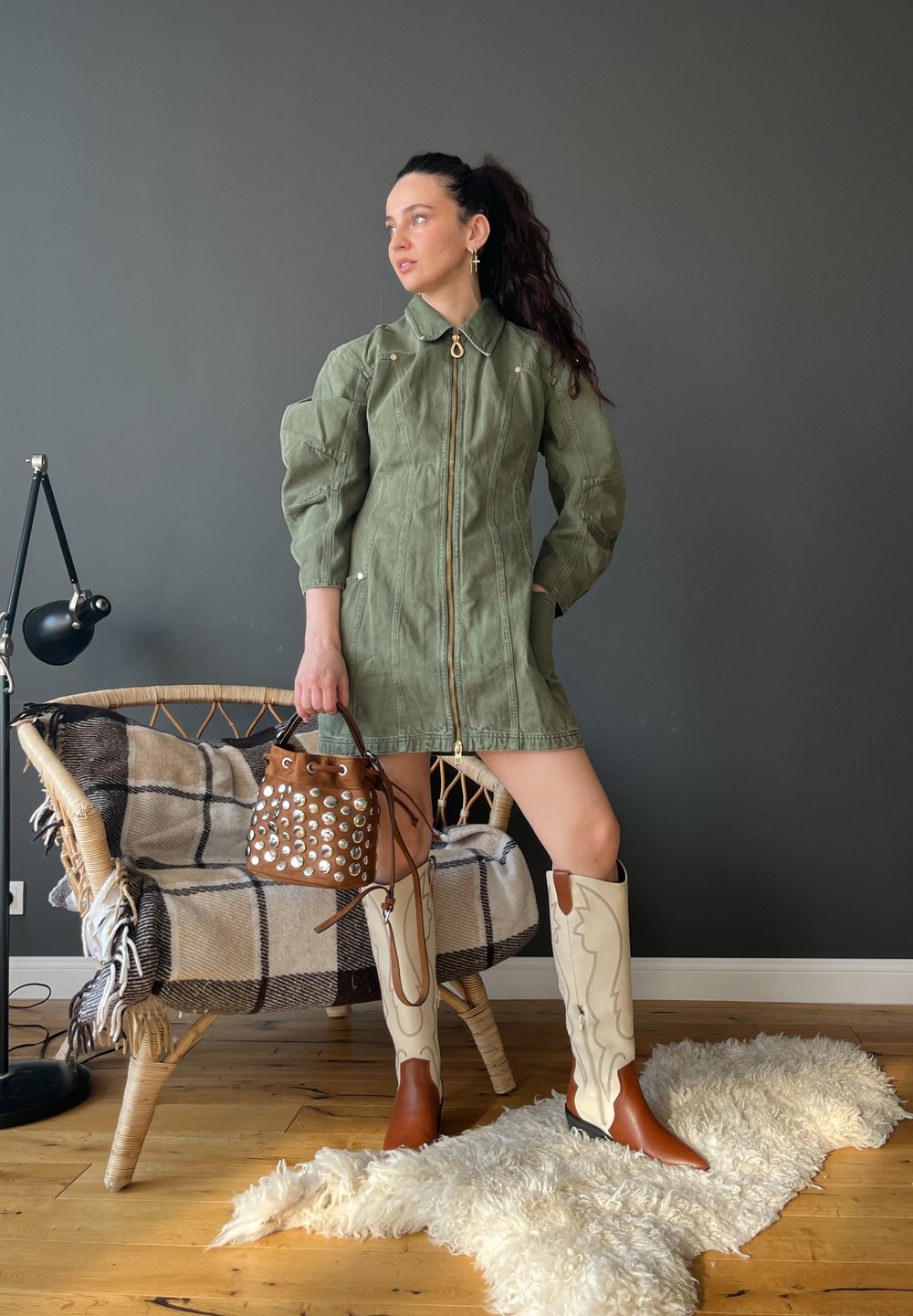 Robe zippée vert olive avec des manches bouffantes, assortie à un sac à main marron clouté et des bottes montantes blanches et marron. Couverture texturée en arrière-plan.