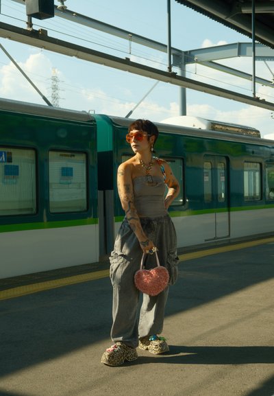 Pantalones cargo grises, blusa gris claro con tirantes, zapatos de leopardo chunky, bolso rosa en forma de corazón, gafas de sol naranjas de gran tamaño. Tren de fondo.