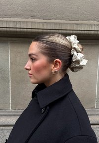 Chouchou à rayures crème, manteau en laine noire avec col cranté, et boucles d'oreilles en forme d'étoile. Cheveux lisses coiffés en chignon.