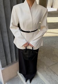 Witte getailleerde blazer met lange mouwen, zwarte riem in de taille, gecombineerd met zwarte wijde broek en een kleine zwarte handtas.