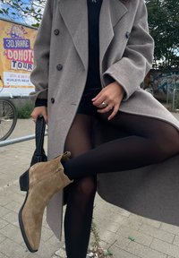 Hall halli villane mantel suurte nuppudega, must ülemine osa, teksashortsid, mustad sukkpüksid ja beežist nahast tikk-kontsa ankle boots, millel on külgne lukk.