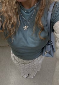 Teal tilpasset skjorte, sølv stjerne halskjede, hvit blonde nederdel med blomstermønster, og lyseblå håndveske med perle detaljer.