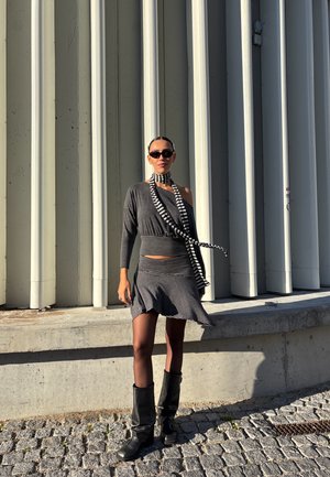 Conjunto de dos piezas a rayas en gris con un top off-shoulder y falda acampanada, combinado con botas negras hasta la rodilla y una bufanda a rayas.