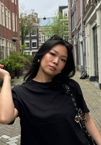 T-shirt en coton noir à manches courtes, porté avec un sac noir présentant un accent décoratif marron et crème. Cadre de rue décontracté.