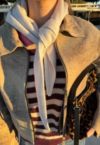 Veste en daim beige portée sur un pull rayé bordeaux et crème, attachée avec une écharpe en tricot blanche. Sac à main noir avec des accents imprimés léopard.
