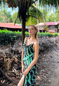 Robe sans manches au design fluide avec des motifs rayés verts et noirs, fabriquée en tissu léger, avec un décolleté drapé et une fente latérale.