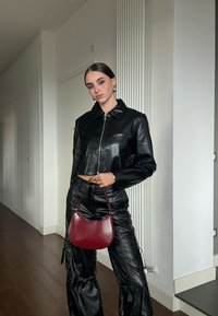 Μαύρο κοντό δερμάτινο μπουφάν με φερμουάρ μπροστά και γιακά, συνδυασμένο με μαύρο δερμάτινο παντελόνι cargo. Κρατάει μια μικρή μπορντό τσάντα.