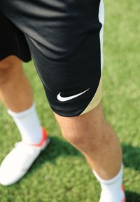 Sorte treningsshorts med gullaccenter, med en hvit Nike-swipe logo. Brukt med hvite sokker og flerfargede fotballsko.