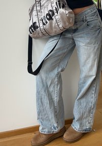 Sac matelassé argenté avec lettrage clouté noir, jean délavé bleu clair et bottines marron. Le sac comporte une bandoulière et des accents métalliques.