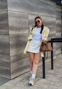 Svijetložuti oversized blejzer preko bijele majice, uparen s bijelom mini suknjom. Smeškan torba i tenisice s uzorkom upotpunjuju izgled.