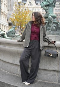 Sivá, textúrovaná bunda cez bordový top; sivé nohavice s vysokým pásom a širokými nohavicami; čierna kabelka so zlatým kovaním; biele topánky.