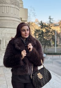 Καφέ τεχνητό παλτό με ψηλό λαιμό, συνδυασμένο με σκούρο πουλόβερ και κολάν με σχέδιο. Μια μαύρη τσάντα με χαρακτηριστικό λογότυπο.