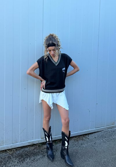 Chaleco de punto negro con rayas blancas, llevado sobre una falda asimétrica blanca. Botas de vaquero negras con detalles de mariposa blanca.