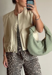 Μπεζ, αμάνικο γιλέκο με φερμουάρ σπροστά και δύο μπροστινές τσέπες. Συνδυασμένο με καφέ παντελόνι με λεοπάρ σχέδιο και πλεκτή πράσινη τσάντα.