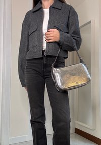 Γκρι κοντό σακάκι με δύο εμπρός τσέπες, φορεμένο πάνω από ένα λευκό πουκάμισο. Συνδυασμένο με ψηλόμεσα μαύρα τζιν και μια μεταλλική ασημένια τσάντα.