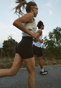 To løpere på en sti; den ene har på seg en lett tank topp og svarte shorts, den andre en hvit ermeløs skjorte og svarte shorts. Skoene er synlige.