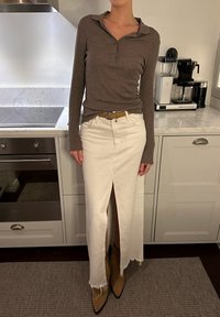 Καφέ μακρυμάνικο πόλο μπλουζάκι, λευκή τζιν φούστα με μπροστινή σχισμή, φθαρμένο στρίφωμα και μπεζ ankle boots με μυτερή μύτη. Ζώνη με κυκλικό κούμπωμα.