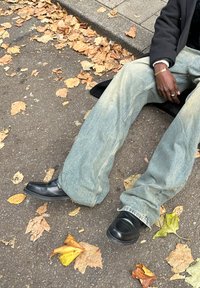 Svetlomodré široké džínsy s rozstrapkanými okrajmi, kombinované s čiernymi nazúvacími topánkami. Okolo sú hnedé a žlté jesenné listy na chodníku.