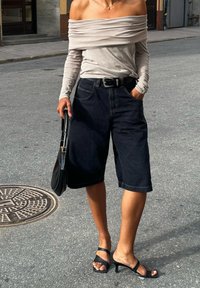 Μπεζ τοπ off-the-shoulder, μαύρες τζην βερμούδες, μαύρη ζώνη και μαύρες πέδιλες με τακούνι. Λείες υφές, άνετο σχέδιο.