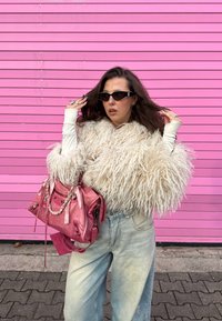 Nažehlená bílá texturovaná bunda, růžová kožená kabelka, sv�ětle modré džínové kalhoty, černé sluneční brýle na růžovém pozadí.