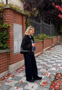 Must jakk sinise kampsuni peal, koos laia säärega tumedate teksade ja mustade kingadega. Õlal ripub must käekott. Maapinda katavad punased ja oranžid lehed.