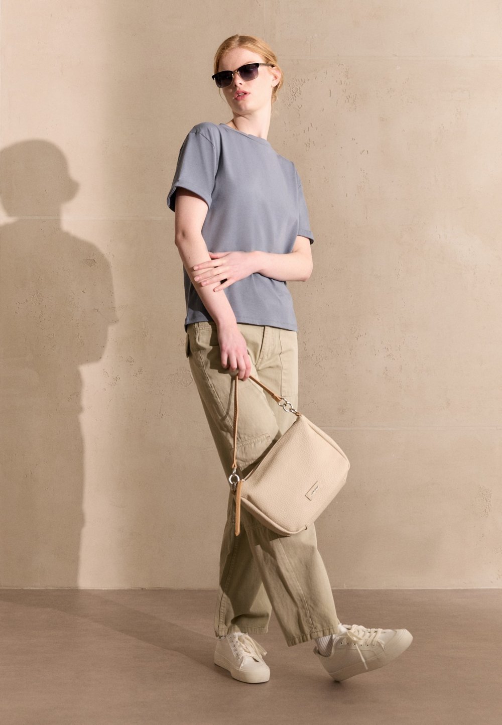 Graues Kurzarm-T-Shirt, hellgrüne Cargo-Hose, weiße Sneakers und eine beiges strukturiertes Handtasche mit Schultergurt. Schwarze Sonnenbrille getragen.