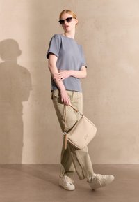 Graues Kurzarm-T-Shirt, hellgrüne Cargo-Hose, weiße Sneakers und eine beiges strukturiertes Handtasche mit Schultergurt. Schwarze Sonnenbrille getragen.