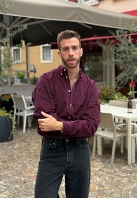 Bordeauxrode corduroy blouse met knoopsluiting, gecombineerd met hoge taille zwarte jeans. Natuurlijke omgeving met tafels en groen op de achtergrond.