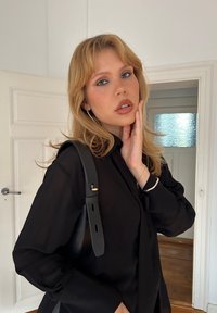 Maglietta nera a maniche lunghe con vestibilità comoda, abbinata a una borsa a spalla nera con tracolla corta. Tessuto liscio e design semplice.