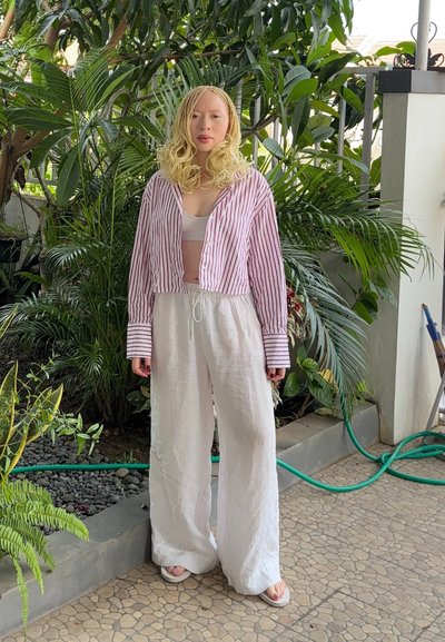 Pantalones anchos de lino blanco, camisa de botones corta a rayas rojas y blancas, y sandalias claras, en medio de exuberantes plantas verdes.